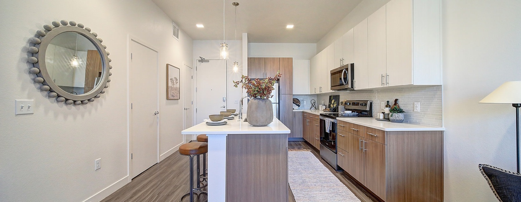 Modern apartment kitchen in Lakewood, CO with wood-style flooring, quartz island, stainless steel appliances, and two-tone cabinetry.