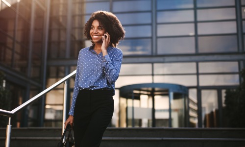 business woman talking on the phone walking out of building