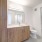 Modern bathroom with walk-in closet, wood-grain cabinets, and white counters.