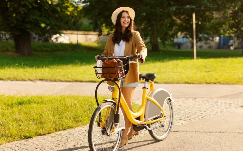 Smiling woman in straw hat riding yellow bike on sunny park path